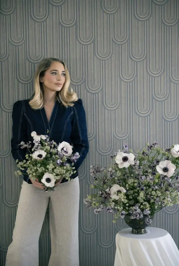 Woman holding a bouquet of white and purple flowers against patterned wallpaper.